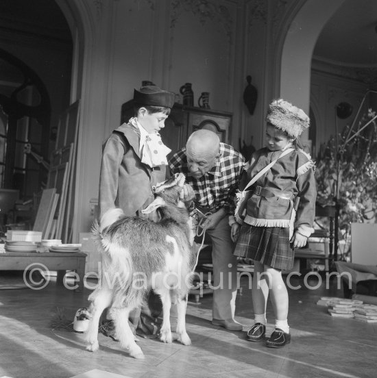 Pablo Picasso with Claude Picasso dressed up as a clown. Paloma Picasso is wearing the Davy Crockett outfit she received as a Christmas present. With goat Esmeralda. La Californie, Cannes 1956. - Photo by Edward Quinn