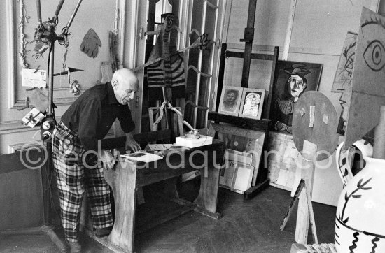 Pablo Picasso sitting at a school bench. Dressed in the checkered trousers that amuse him because of their association with the self-portraits of Courbet. La Californie, Cannes 1957. - Photo by Edward Quinn