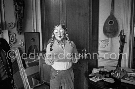 Clown scene: Pablo Picasso in drag, wearing a carnival mask. In the background two masks (1956) by Pablo Picasso. La Californie, Cannes 1958. - Photo by Edward Quinn