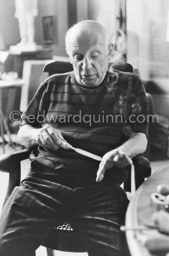 Pablo Picasso feels the sharpness of one of the tools he uses for linocuts. He holds a cigarette at the same time. La Californie, Cannes 1959. - Photo by Edward Quinn