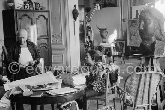 Pablo Picasso correcting "Faunes et chèvres". With Jacqueline (wearing a blouse with Pablo Picasso motifs). A pile of books: Level, André: Souvenirs d'un collectionneur. Avec en frontispice un lithographie originale de Pablo Picasso (les saltimbanques). A.C. Mazo, Paris 15.10.1959. La Californie, Cannes 1959. - Photo by Edward Quinn