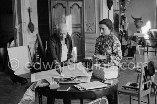 Pablo Picasso correcting "Faunes et chèvres". With Jacqueline (wearing a blouse with Pablo Picasso motifs). A pile of books Level, André: Souvenirs d'un colectionneur. Avec en frontispice un lithographie originale de Pablo Picasso (les saltimbanques). A.C. Mazo, Paris 15.10.1959. La Californie, Cannes 1961. - Photo by Edward Quinn