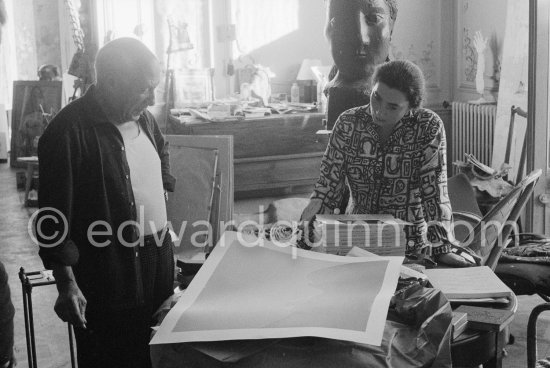 Pablo Picasso correcting a print. With Jacqueline (wearing a blouse with Pablo Picasso motifs). A pile of books Level, André: Souvenirs d'un colectionneur. Avec en frontispice un lithographie originale de Pablo Picasso (les saltimbanques). A.C. Mazo, Paris 15.10.1959. La Californie, Cannes 1959. - Photo by Edward Quinn