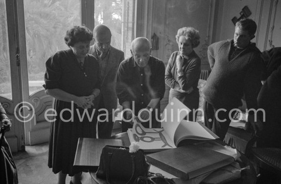 Picasso looks at the copy of a deluxe edition of a book of poems by Pierre Reverdy, for which he has made the illustrations. Gathered around him as he comments on the book are Madame Weill, the writer Michel Leiris, his wife Louise Leiris, owner with Kahnweiler of the Leiris Gallery Paris, and Paulo. La Californie, Cannes 1959. - Photo by Edward Quinn