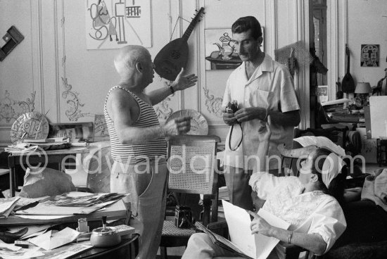 Pablo Picasso, Jacqueline and Edward Quinn viewing photos by Quinn, which the latter brought as a gift. Quinn with his Leica M3, on the chair his Rolleiflex 3.5B. La Californie, Cannes 8.9.1960. Photographer unknown. - Photo by Edward Quinn