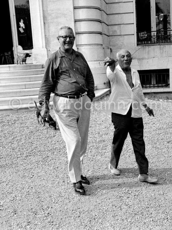 Pablo Picasso with Douglas Cooper and the dogs Lump and Ma Jolie behind Cooper. In front of La Californie, Cannes 1961. - Photo by Edward Quinn