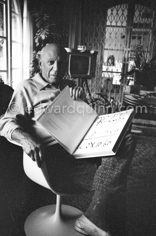 Pablo Picasso with the book "Pablo Picasso at Work" by Edward Quinn, dedicated by Pablo Picasso and Edward Quinn "Pour Jacqueline Kennedy". In the background TV-table by Tiola. Mas Notre-Dame-de-Vie, Mougins 1964. - Photo by Edward Quinn