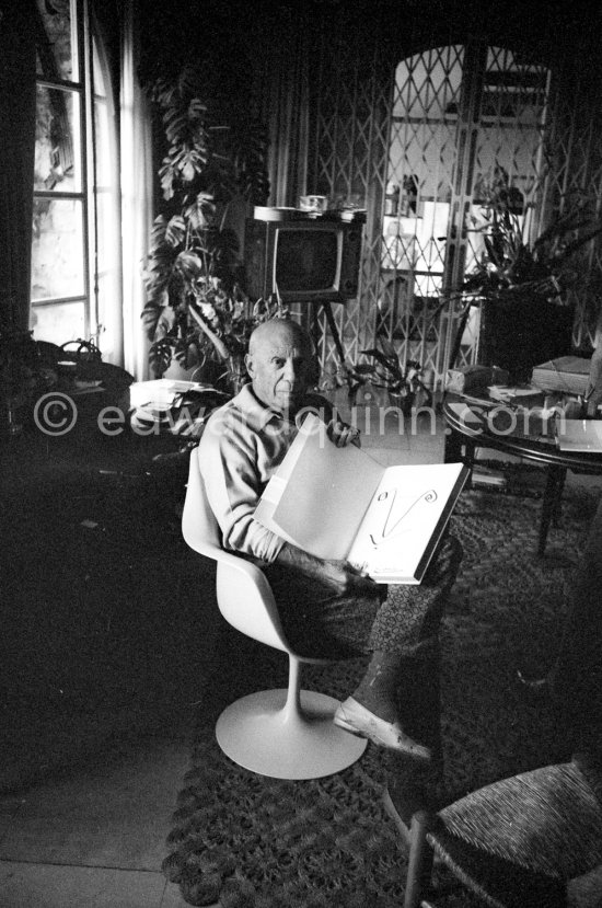 Pablo Picasso with the book "Pablo Picasso at Work" by Edward Quinn, dedicated by Pablo Picasso and Edward Quinn "Pour Jacqueline Kennedy". In the background TV-table by Tiola. Mas Notre-Dame-de-Vie, Mougins 1964. - Photo by Edward Quinn