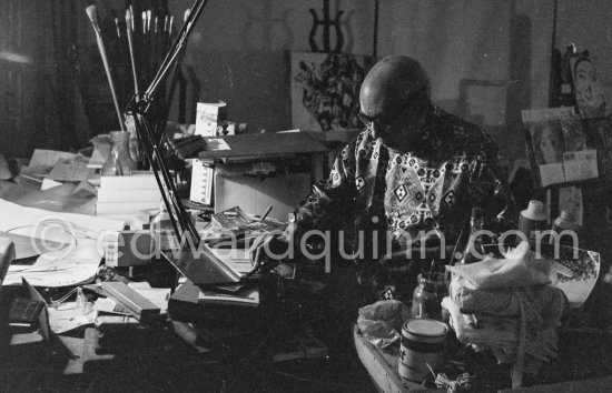 Pablo Picasso at work in a corner of his living room table, engraving his signature on a small lucky dollar coin at a visitor’s request. Visitors usually brought some object or present that they hoped would interest or intrigue Pablo Picasso, and they were seldom disappointed. Mas Notre-Dame-de-Vie, Mougins 1967. - Photo by Edward Quinn