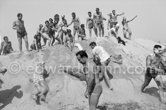 Towards the end of the fifties, Saint-Tropez became very popular for the holiday makers. This was mostly due to the presence of Brigitte Bardot, Roger Vadim, Françoise Sagan. Here young and older and also a little dog (on the right) enjoy themselves on a mountain of sand in a mud battle. Saint-Tropez 1961. - Photo by Edward Quinn