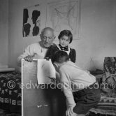 Encouraged by his father, Claude Picasso tries to do a portrait of Pablo Picasso, portraying him with a round face, deep furrows on his forehead, a triangle for a nose, and streaks of hair on the sides of his head. La Galloise, Vallauris 16.4.1953. - Photo by Edward Quinn
