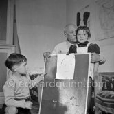 Encouraged by his father, Claude Picasso tries to do a portrait of Pablo Picasso, portraying him with a round face, deep furrows on his forehead, a triangle for a nose, and streaks of hair on the sides of his head. La Galloise, Vallauris 16.4.1953. - Photo by Edward Quinn