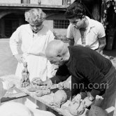 Pablo Picasso with some of the ceramic figures he made in clay, before they are put in the kiln. With him is Suzanne Ramié of the Madoura pottery. Suzanne is wearing a pendant by Pablo Picasso. Outside Madoura pottery, Vallauris 1953. - Photo by Edward Quinn