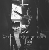 During filming of "Le mystère Picasso". Pablo Picasso working on "Nature morte". Pablo Picasso had a frame constructed on which he could stretch a transluscent piece of paper. He drew on one side, and the camera filmed the drawing being born from the other side. Nice, Studios de la Victorine 1955. - Photo by Edward Quinn