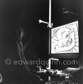 During filming of "Le mystère Picasso". Pablo Picasso working on "Tête de femme" with colored ink. He had a frame constructed on which he could stretch a transluscent piece of paper. He drew on one side, and the camera filmed the drawing being born from the other side. Nice, Studios de la Victorine 1955. - Photo by Edward Quinn