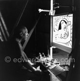 During filming of "Le mystère Picasso". Pablo Picasso working on "Tête de femme" with colored ink. He had a frame constructed on which he could stretch a transluscent piece of paper. He drew on one side, and the camera filmed the drawing being born from the other side. Nice, Studios de la Victorine 1955. - Photo by Edward Quinn