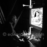 During filming of "Le mystère Picasso". Pablo Picasso working on "Tête de femme" with colored ink. He had a frame constructed on which he could stretch a transluscent piece of paper. He drew on one side, and the camera filmed the drawing being born from the other side. Nice, Studios de la Victorine 1955. - Photo by Edward Quinn