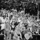 Pablo Picasso on the grandstand at the corrida surrounded by his family and friends. Lartigue and his wife Florette, Vilató and wife Germaine Lascaux, Jacqueline, Maya Picasso, Jean Cocteau, Francine Weisweiller, Dr. Jeanne Creff (acupuncturist of Pablo Picasso), with the guitar the son of the writer José Herrera-Petere. Vallauris 1955. - Photo by Edward Quinn