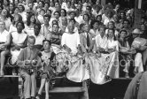 On the grandstand of a bullfight put on in Pablo Picasso's honor. On the left of Pablo Picasso Jacqueline, on the right Jean Cocteau, Inès Sassier, Pablo Picasso's housekeeper and Francine Weisweiller and her daughter Carole, behind Pablo Picasso his children Paloma Picasso, Maya Picasso and Claude Picasso, in front on the left photographer Jacques-Henri Lartigue, loading a film in his Rolleiflex, and his wife Florette. Vallauris 1955. - Photo by Edward Quinn