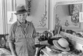 To strike a pose, Pablo Picasso tries on hats from his collection for his own amusement and that of his guests. La Californie, Cannes 1956. - Photo by Edward Quinn