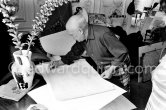 Pablo Picasso signing "Faune debout jouant de la diaule, nymphe assise au tambourin et au compotier de fruits, et centaure barbu au trident IV" or "Faune jouant de la diaule, nymphe au compotier et centaure" (Suite Antipolis), 1946. La Californie, Cannes 1957. - Photo by Edward Quinn