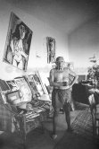 Behind Pablo Picasso a large sofa weighed down with an array of papers, prints, tennis rackets, hats. Mas Notre-Dame-de-Vie, Mougins 1964. - Photo by Edward Quinn